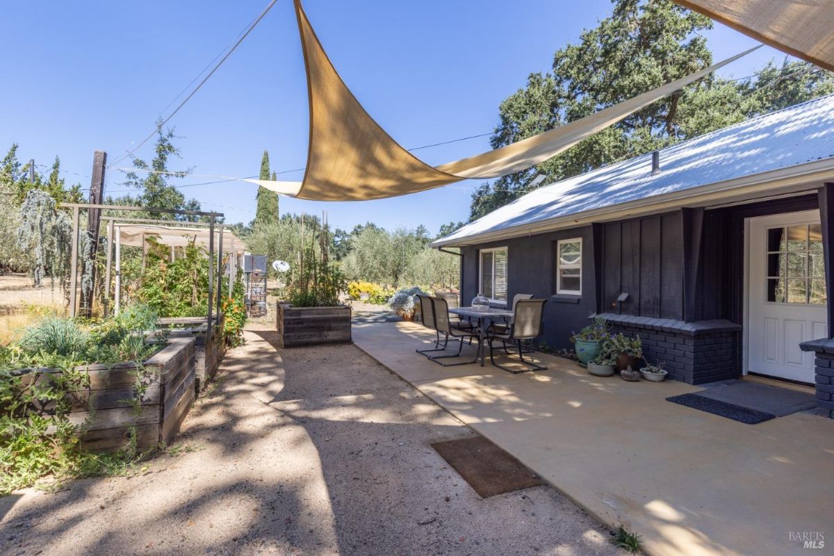 Side yard features raised garden beds, outdoor seating, and sunshade sails.