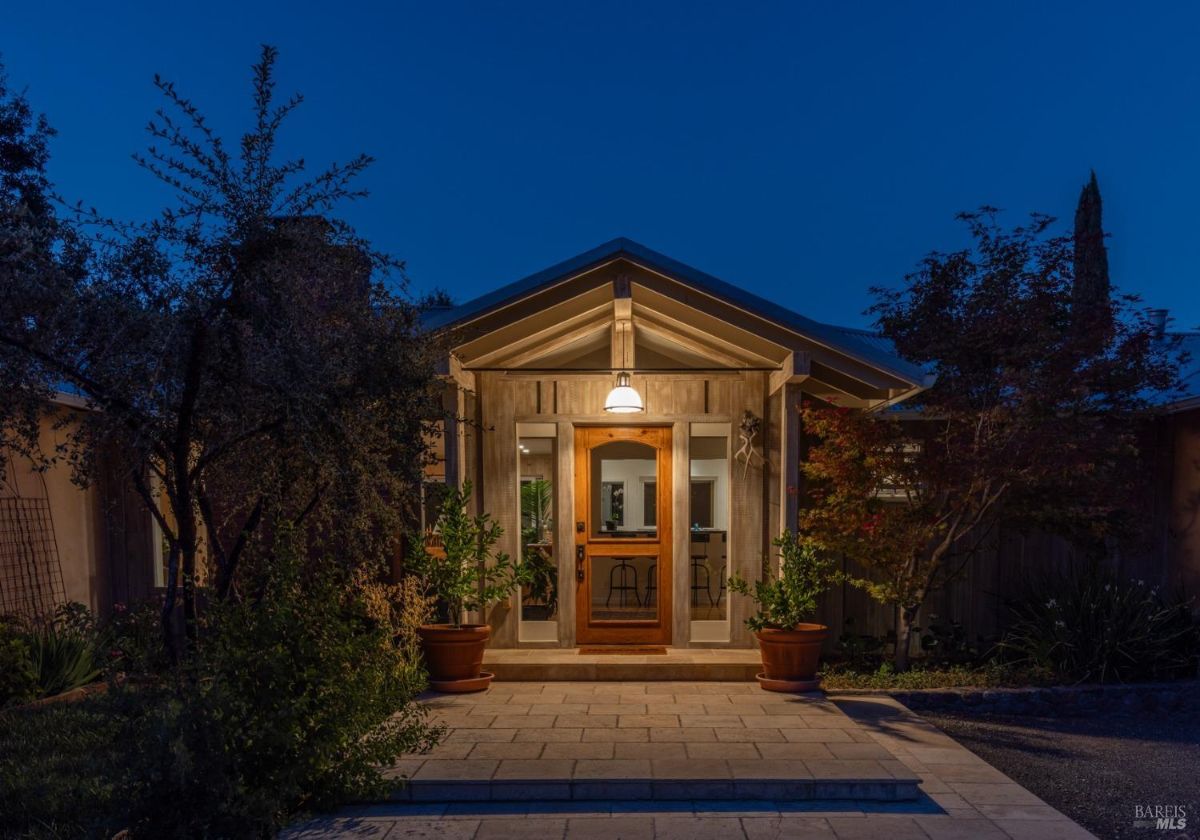 Evening shot of a house entrance with a warmly lit wooden door and potted plants.