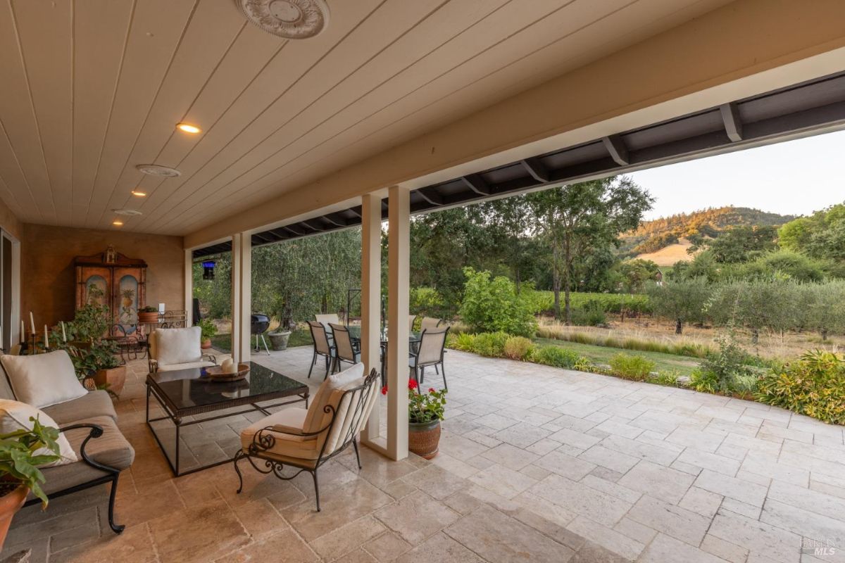 Outdoor patio area features seating with a covered ceiling and views of greenery and hills.