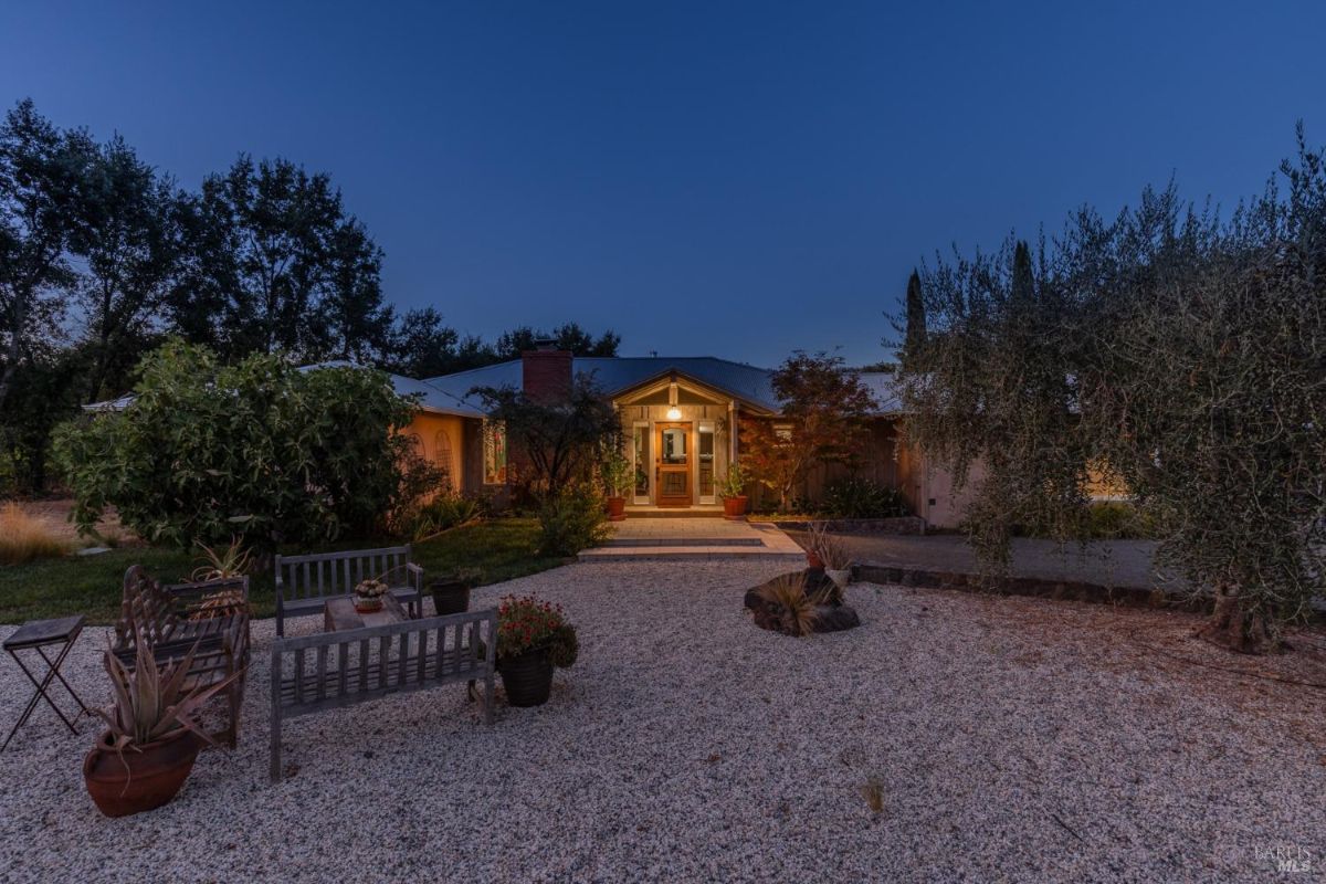 Evening view of the house highlights illuminated windows and gravel landscaping with outdoor seating.