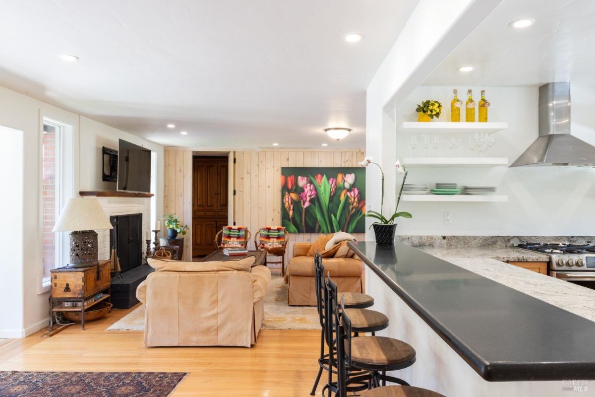 Living room with a fireplace, light furniture, and a bar-style countertop adjacent to a colorful tulip painting.