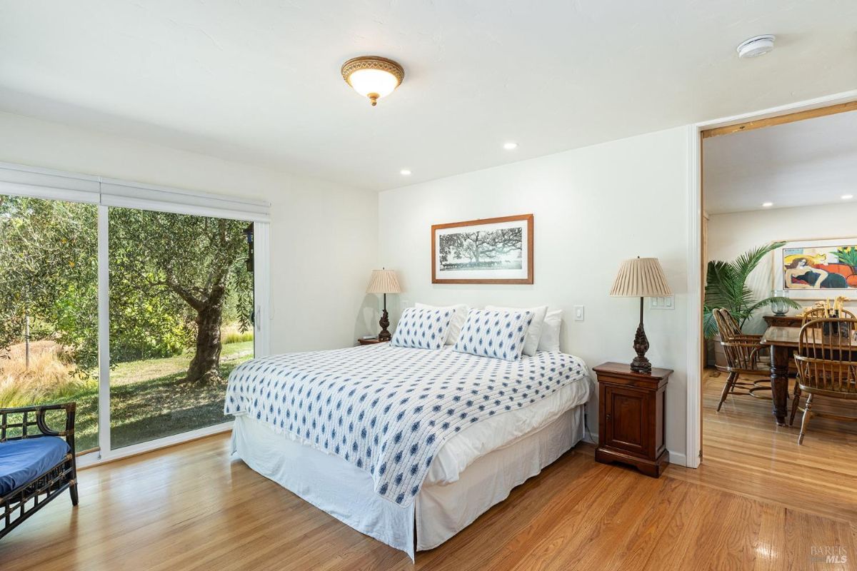 Bedroom with a blue-patterned bedspread, wooden flooring, and a sliding glass door leading to an outdoor area