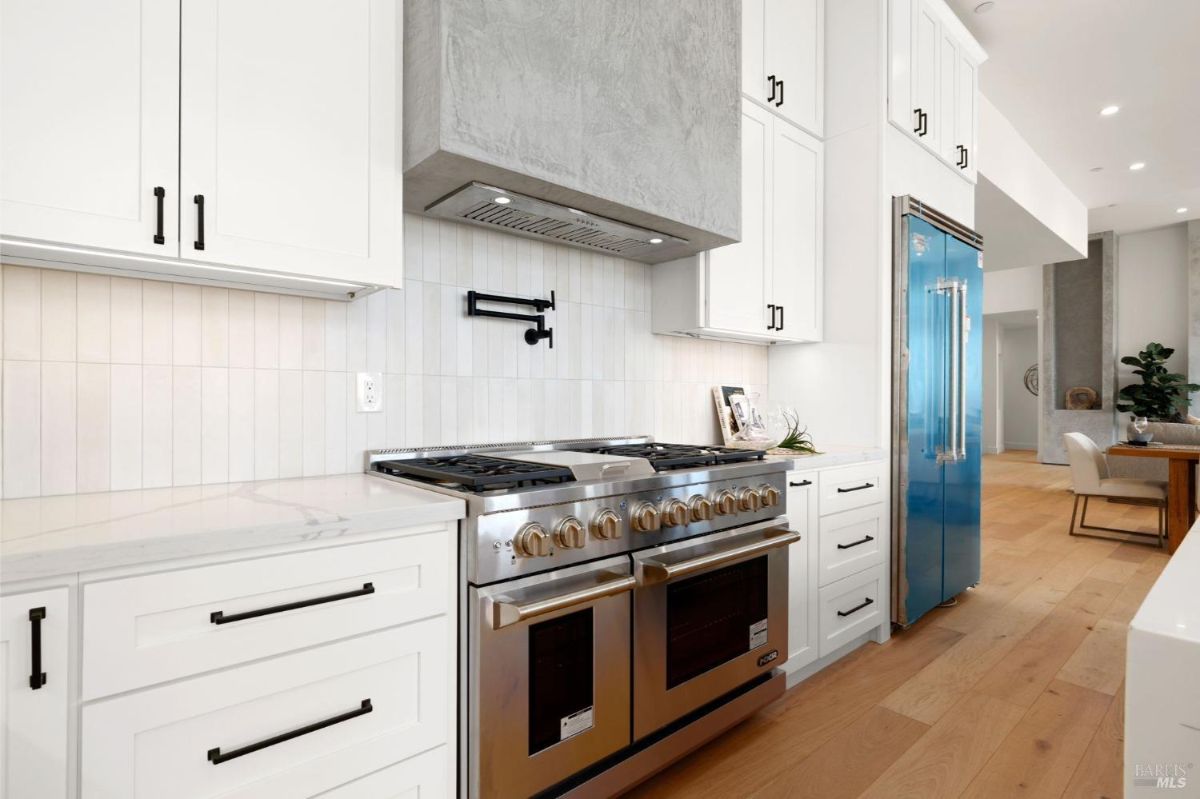 Stainless steel double oven and gas range with a modern hood installed in a white kitchen.