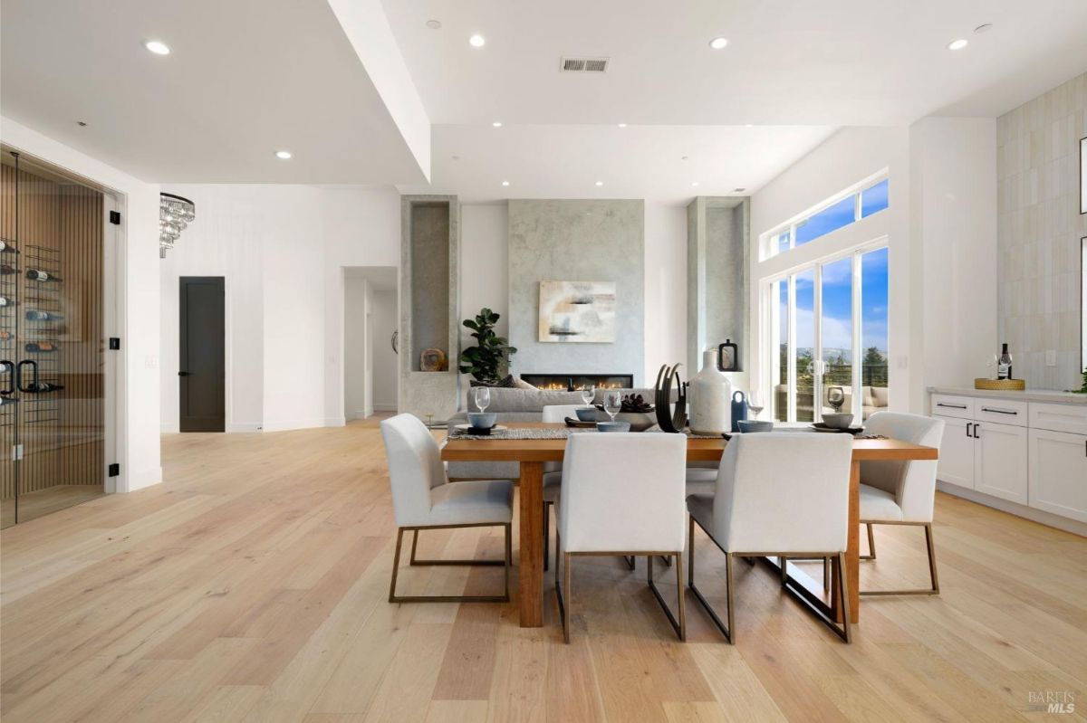 Dining area with a wooden table, white chairs, and large windows allowing natural light.