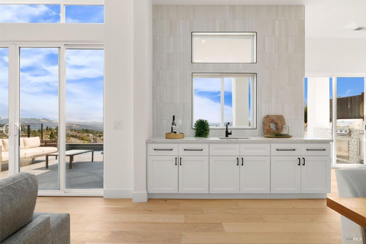 Wet bar with a sink, white cabinets, and access to a patio area