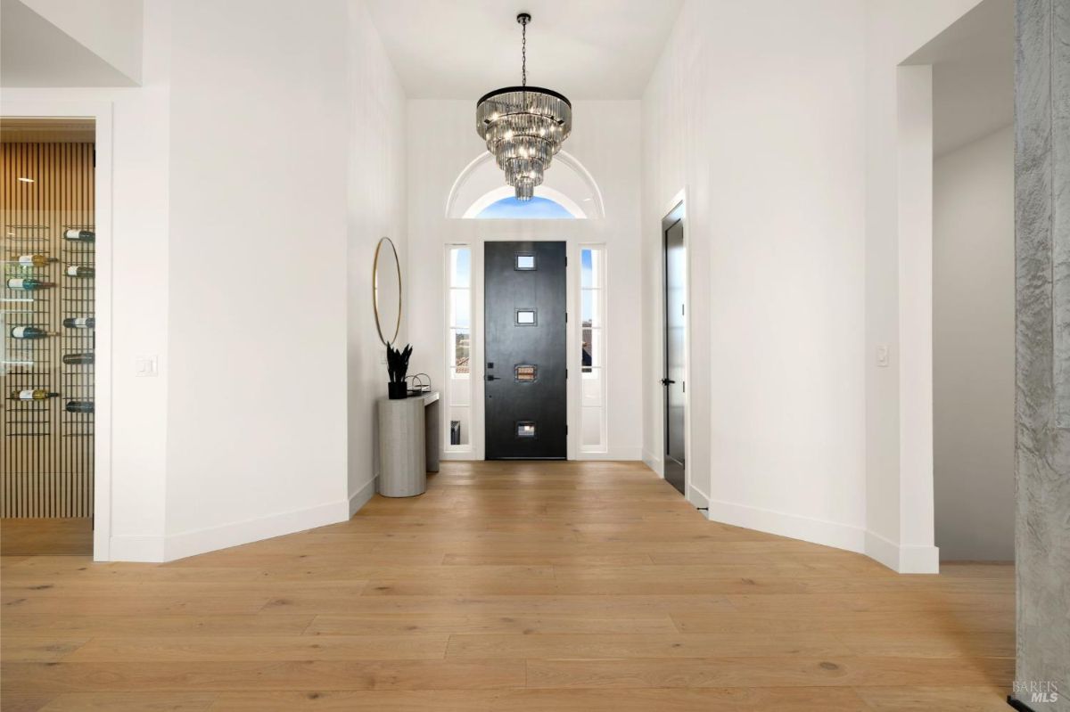 Entryway with wooden floors, a modern chandelier, and a dark front door.