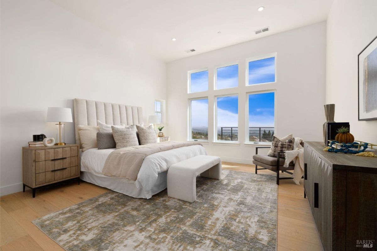 Master bedroom with large windows, high ceilings, and modern furniture.