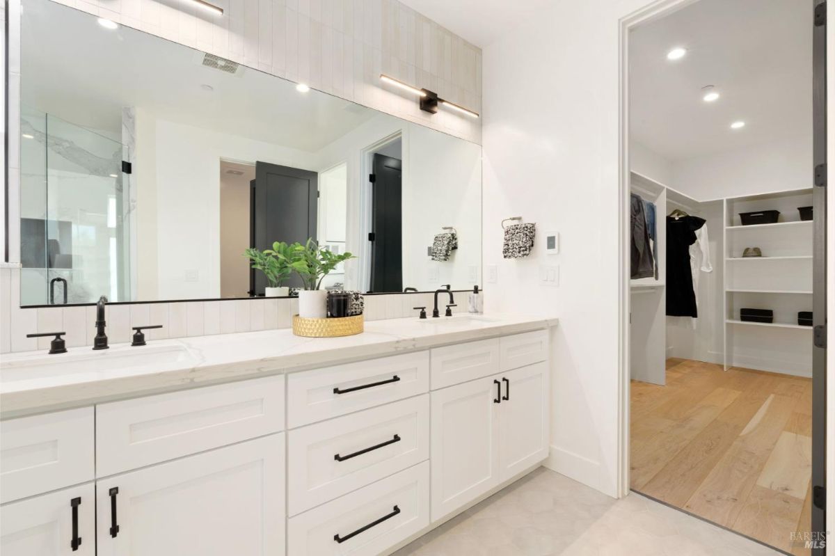 Master bathroom featuring a double vanity, large mirror, and entrance to a walk-in closet.