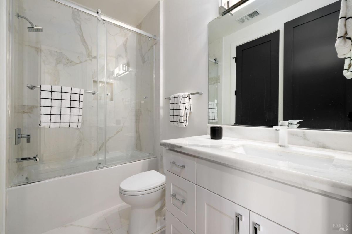 Bathroom with a marble shower, sliding glass doors, and white cabinetry.