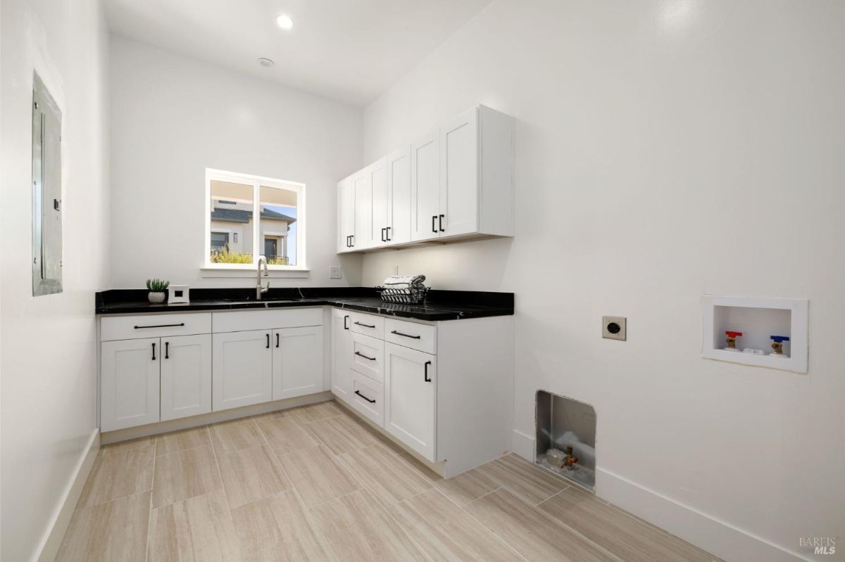 Laundry room with white cabinetry, black countertops, and tile flooring.