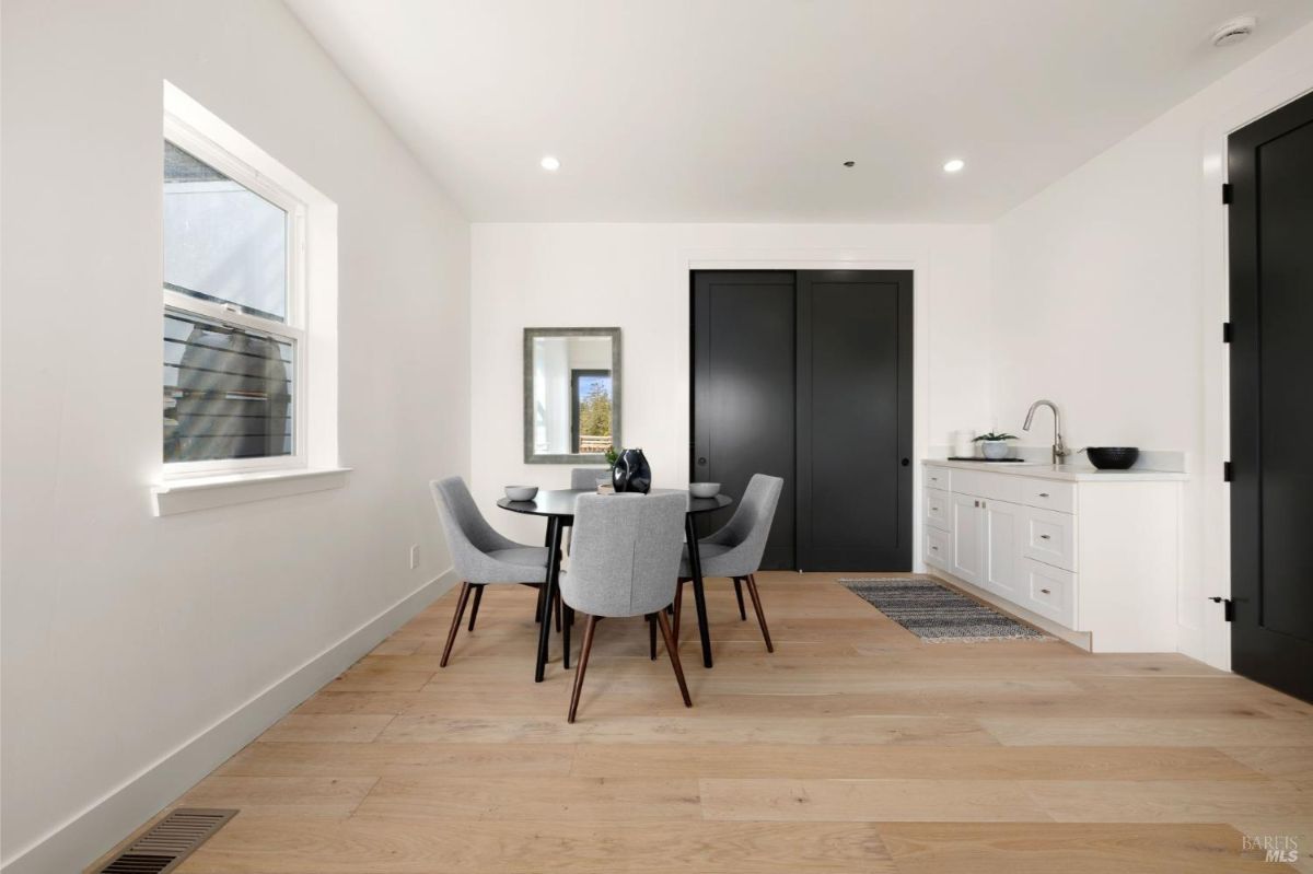 Small dining nook with a black round table, gray chairs, and a kitchenette in the corner.